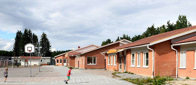 Skolgården vid Slottsskolan i Skokloster med basketkorg, lekande barn och skolbyggnaden i rött tegel