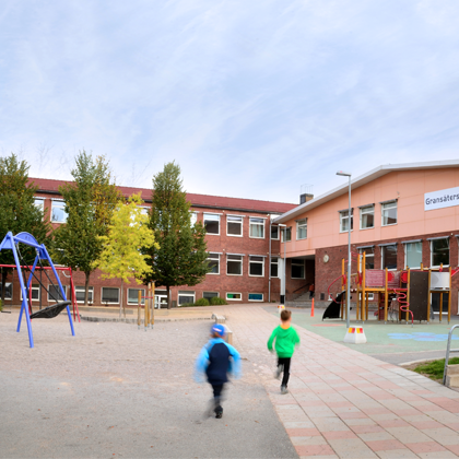 Skolgården vid Gransäterskolan i Bålsta med gungor, klätterställning och skolbyggnaden i rött tegel