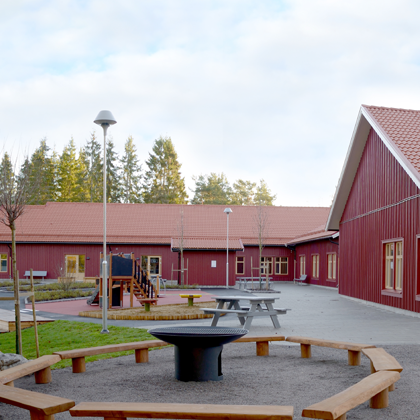 Slottsbackens förskola – röda byggnader med gård, bänkar och eldstad