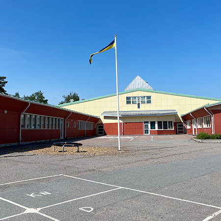 Västerängsskolans skolgård i Bålsta med svensk vimpel, lek- och aktivitetsytor och skolbyggnaden i rött och gult